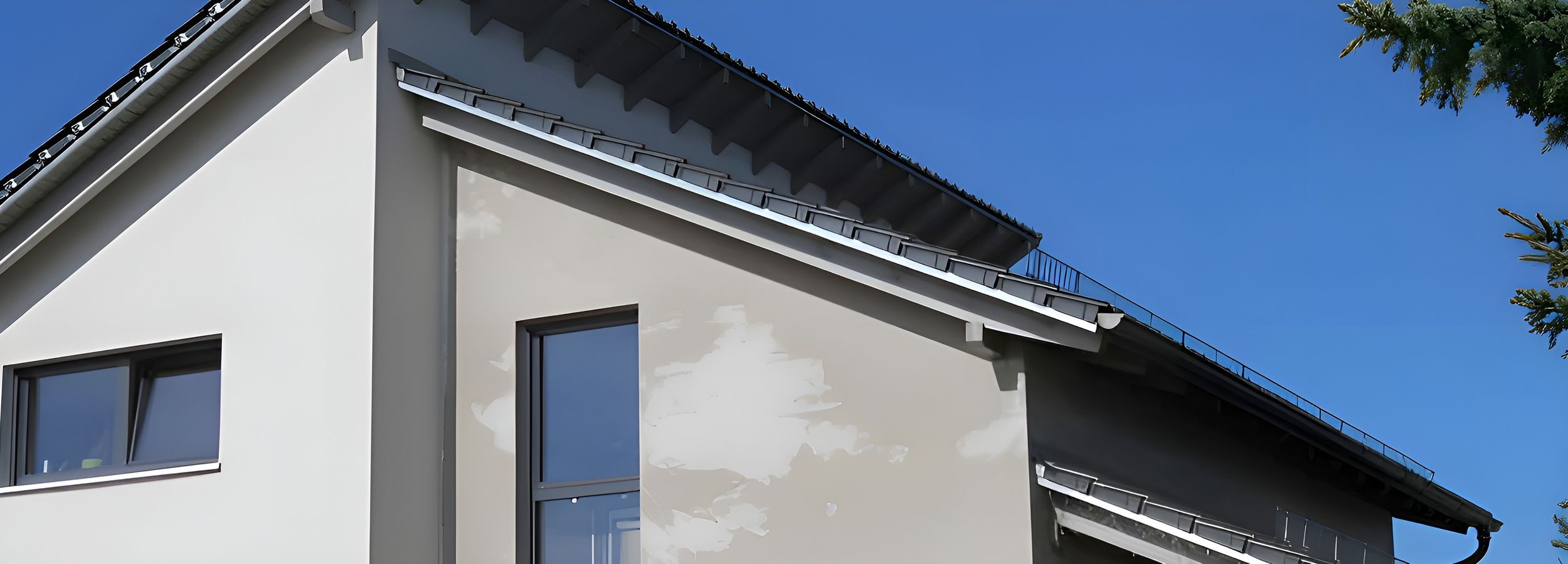 Modernes Einfamilienhaus mit weißer Fassade und dunklem Satteldach unter blauem Himmel